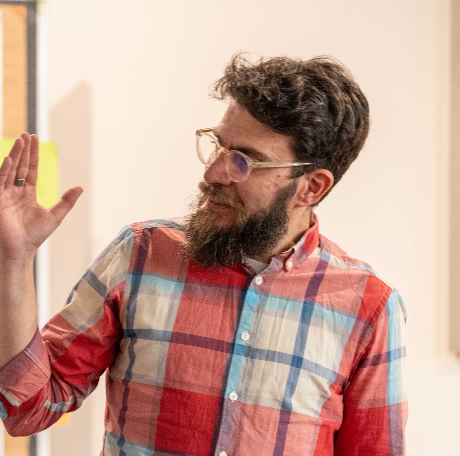 Consultant in a checked shirt gesturing and looking back at a pinboard