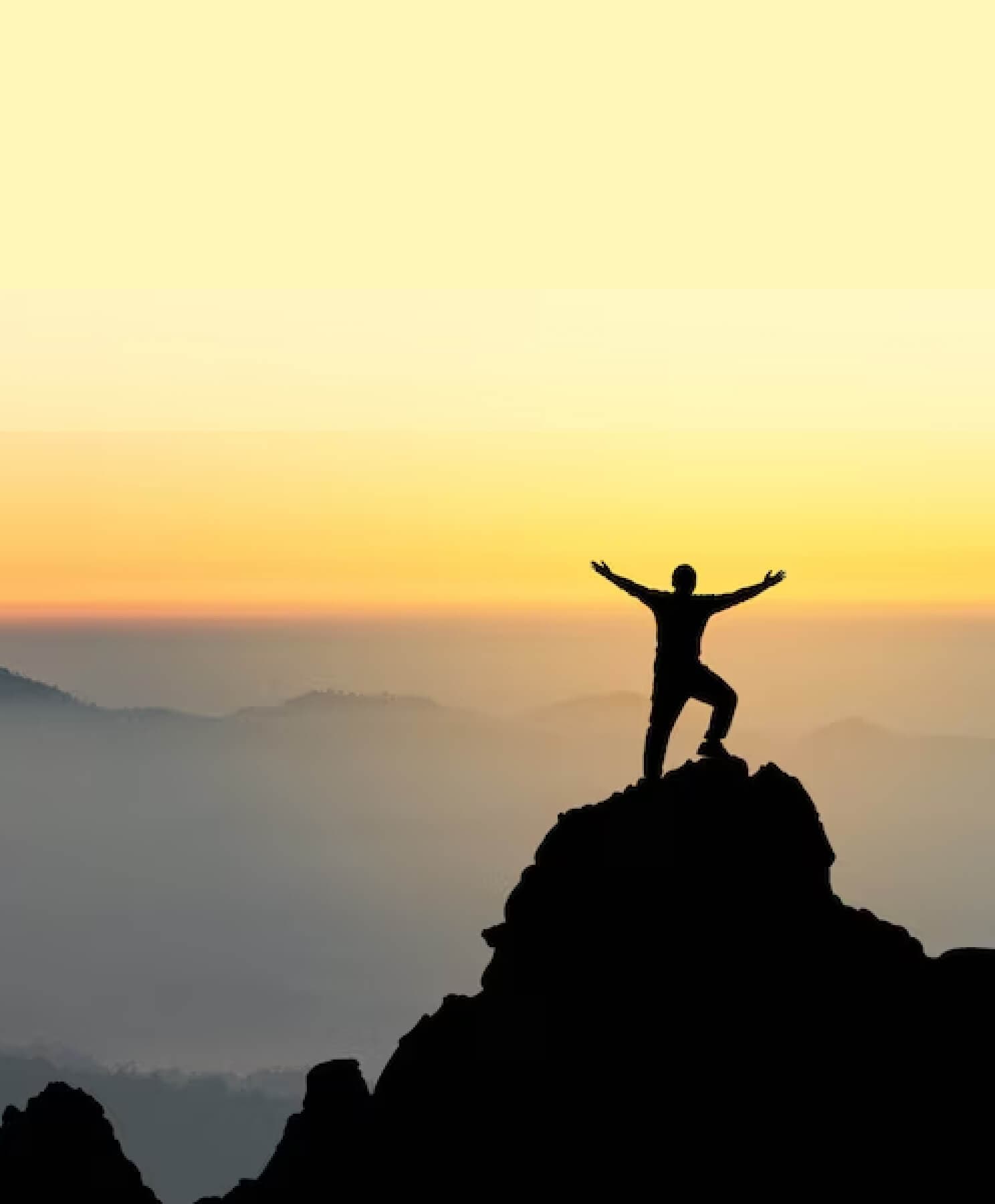Silhouette einer Person mit erhobenen Armen auf einem Berggipfel bei Sonnenaufgang