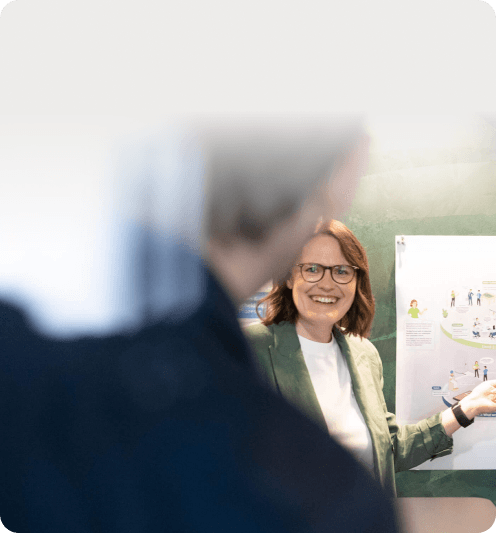 Smiling woman in a green blazer in front of an illustrated poster on corporate culture