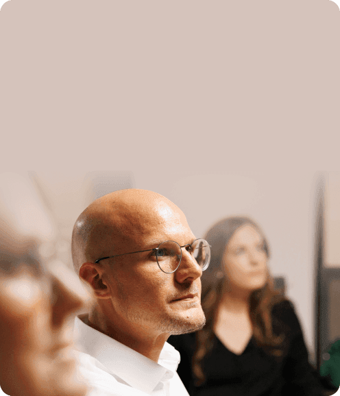 Leader with glasses in conversation, a listening colleague behind him