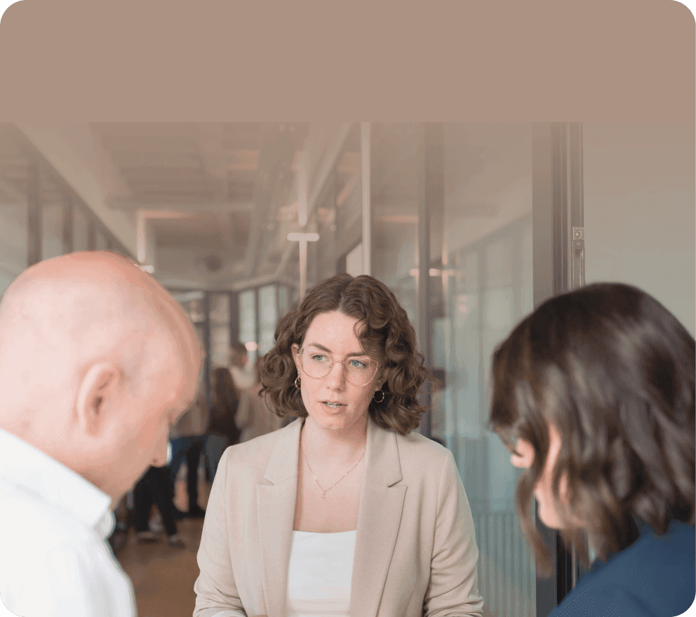 Woman in a beige blazer talking with two colleagues in an office corridor