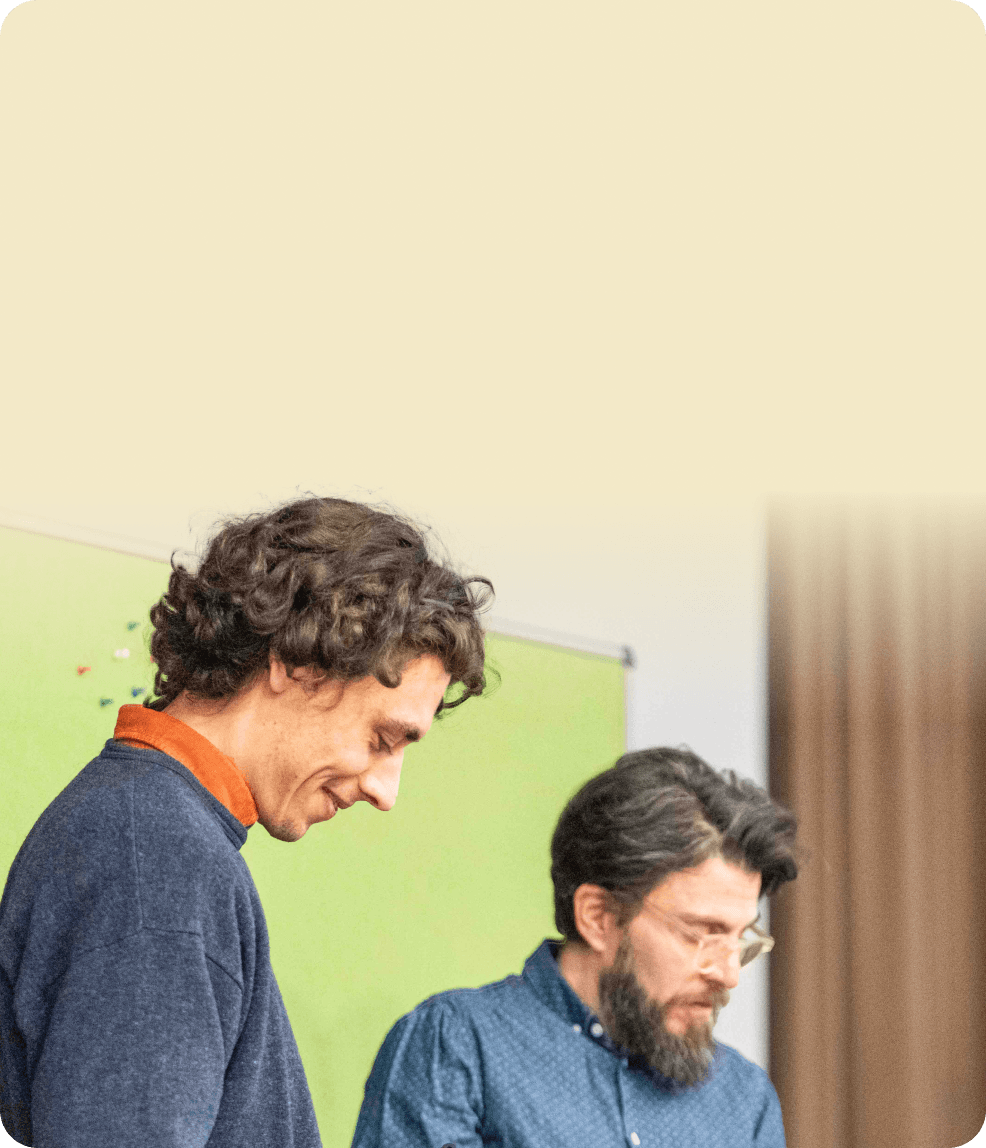 Two colleagues looking down at documents together in front of a green pinboard