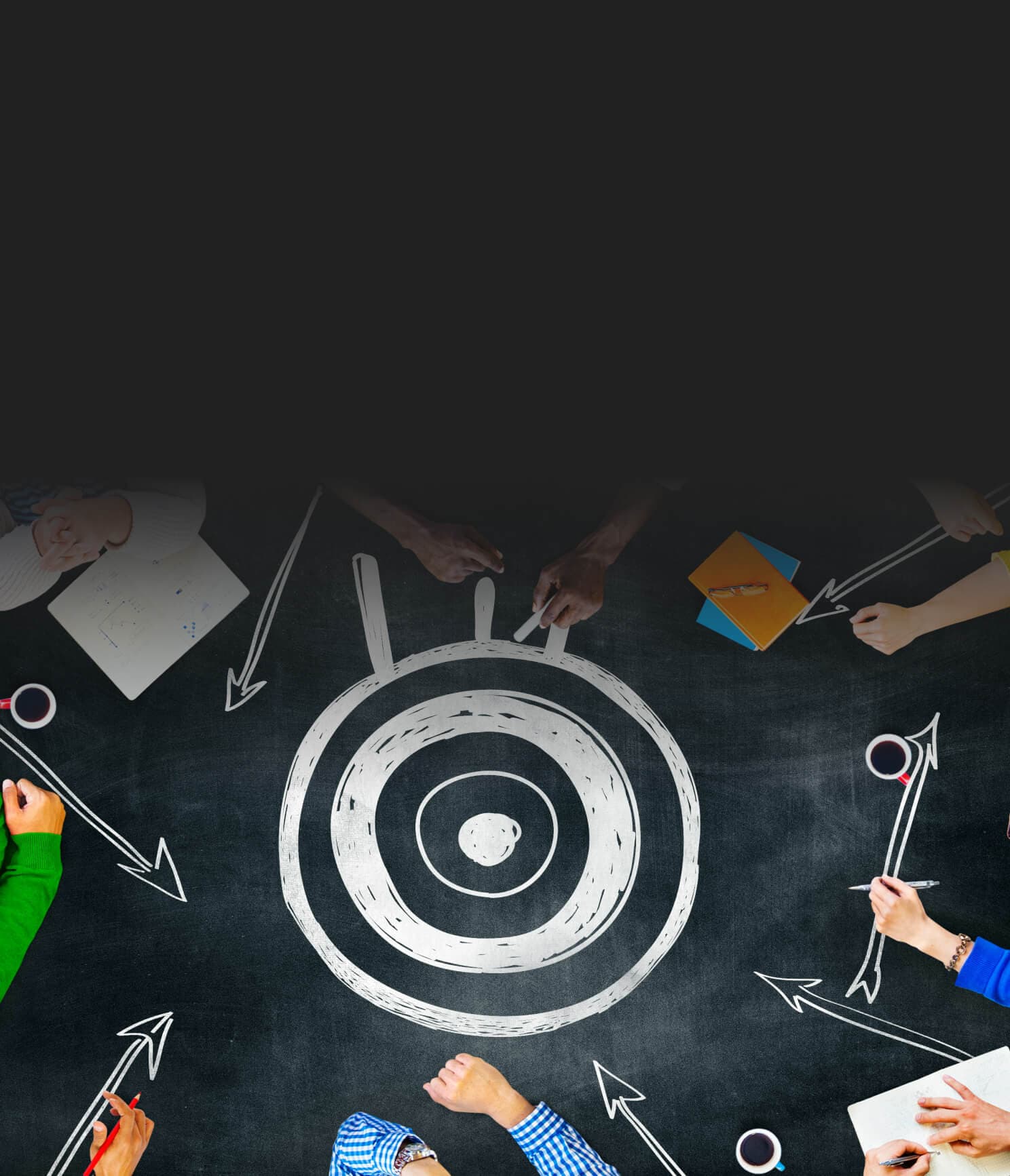 Target drawn on a chalkboard, surrounded by hands and arrows – goals broken down into steps