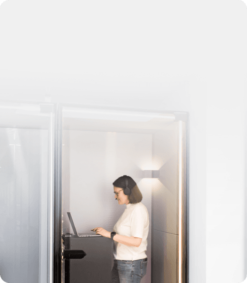 Woman with a headset working on a laptop in a glass phone booth