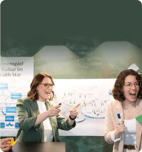 Two women cheering and laughing in front of culture posters in a workshop room