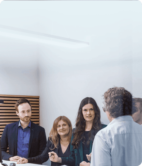 Team at a meeting table: one colleague explains, the others listen