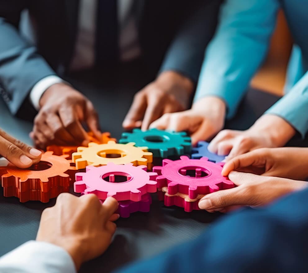 Several hands fitting colorful wooden gears together on a table