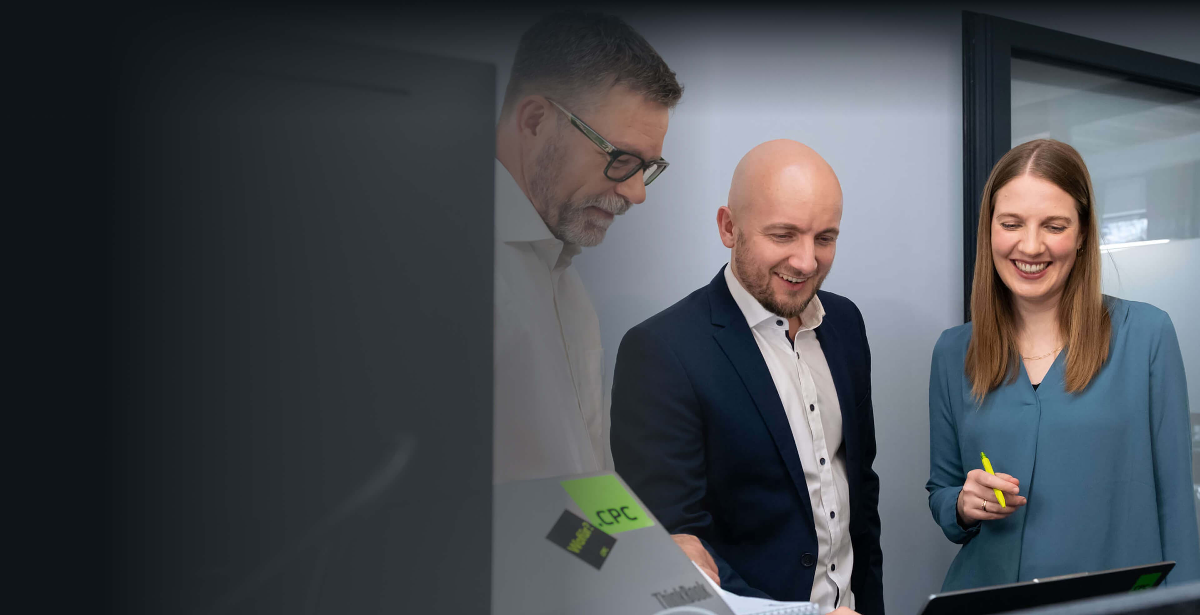 Consultant with a highlighter and two colleagues smiling as they discuss the AI strategy on a laptop