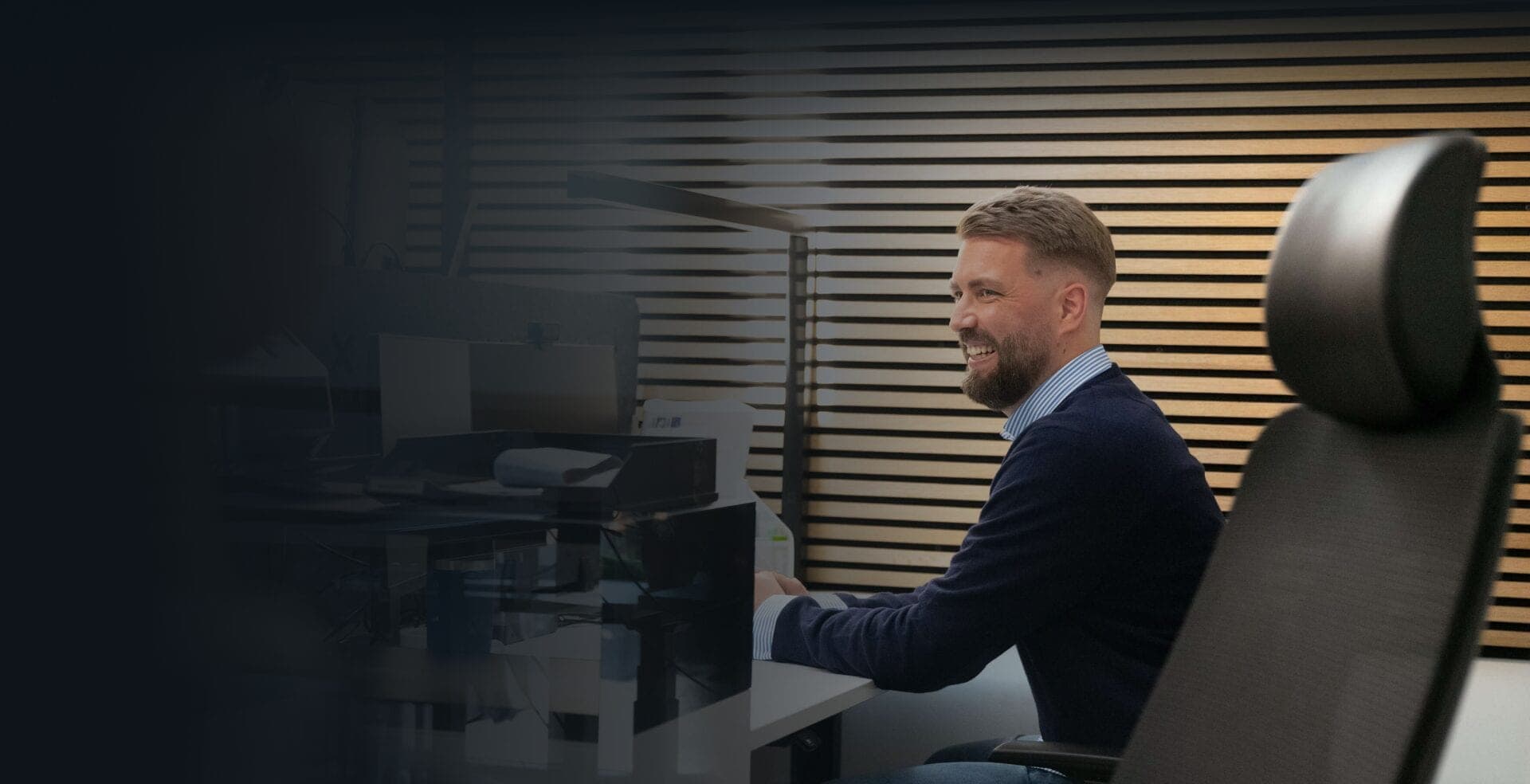 Smiling employee working at his desk in front of a wooden slat wall