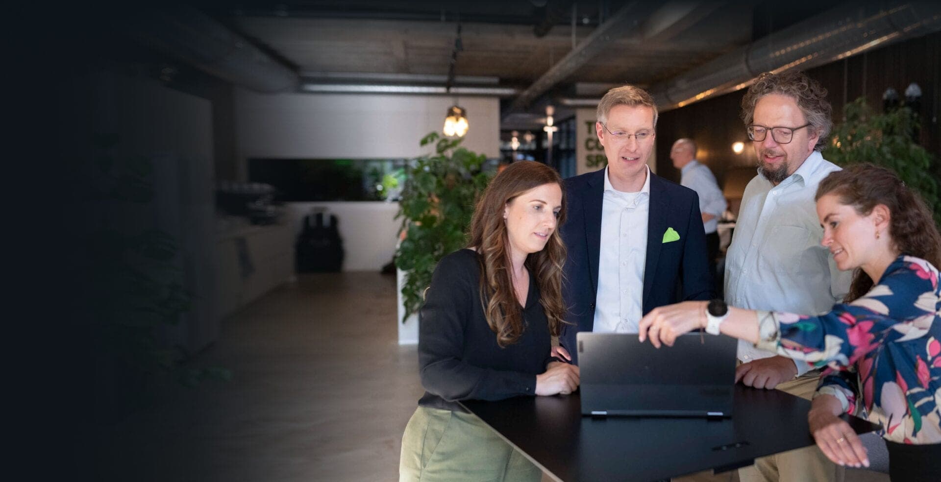 Four colleagues at a standing table discussing content on a laptop