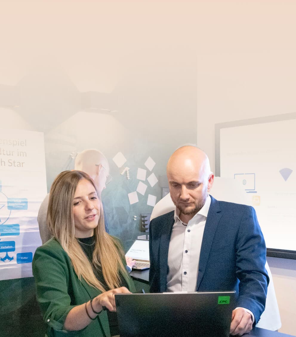 Consultant going through the next steps with a colleague on a laptop, with workshop posters behind them