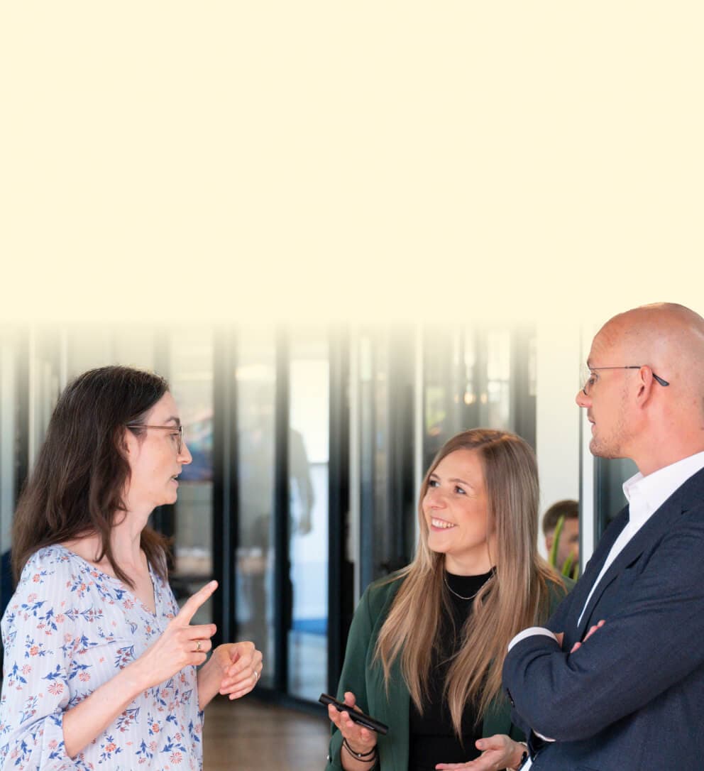 Consultant in discussion with two colleagues in the glass-walled corridor of an office