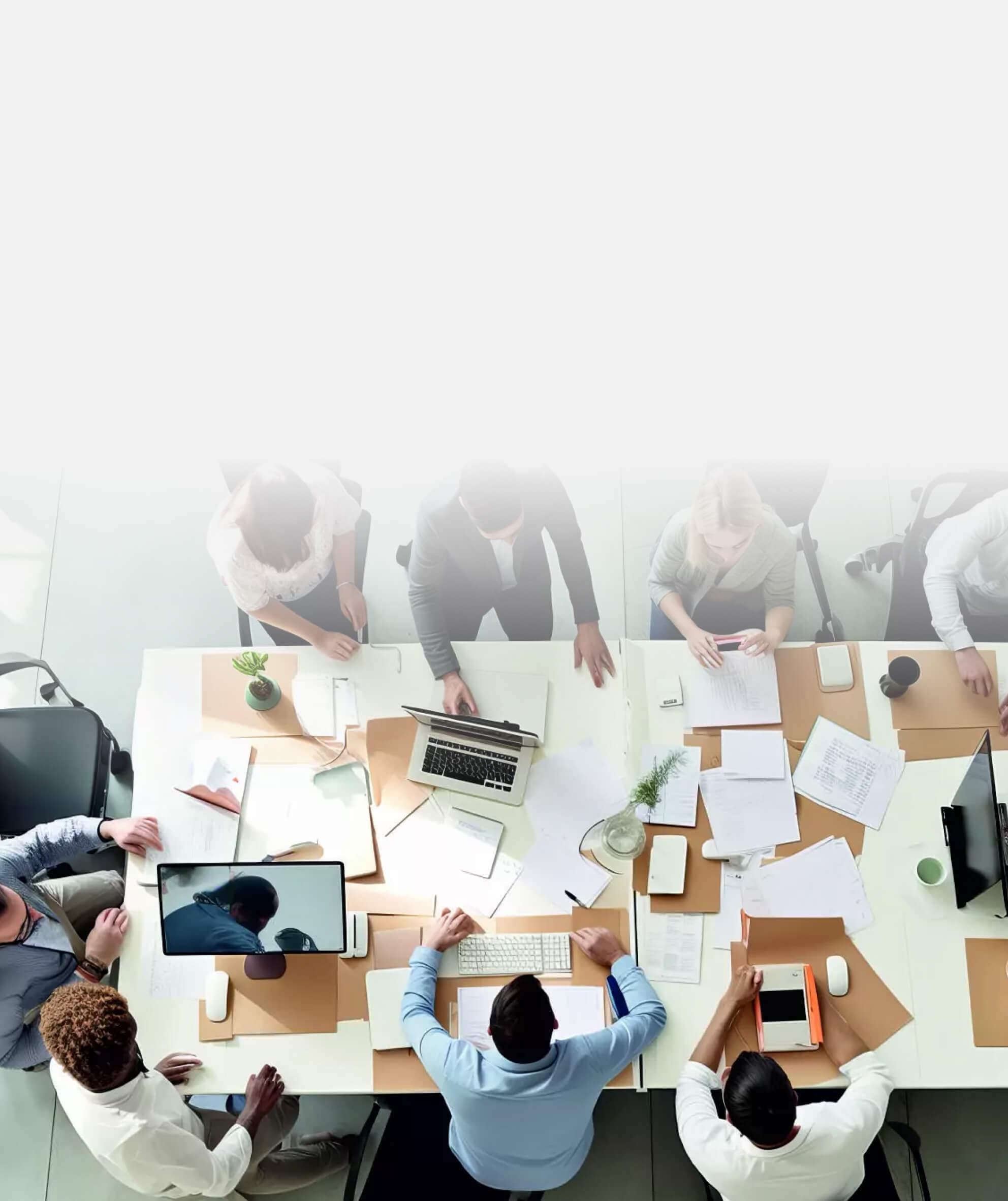 Blick von oben auf ein Team, das an einem großen Tisch mit Laptops und Unterlagen arbeitet