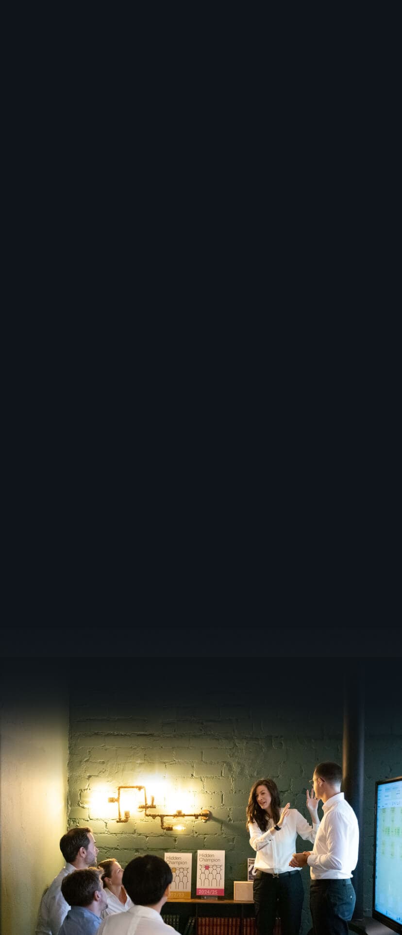 Trainerin präsentiert vor einer Gruppe im Seminarraum, im Hintergrund Hidden-Champion-Auszeichnungen und ein Bildschirm