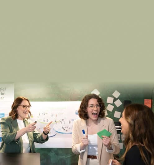 Teilnehmerinnen lachen in einem Workshop vor einer Stellwand mit Visualisierung und Moderationskarten