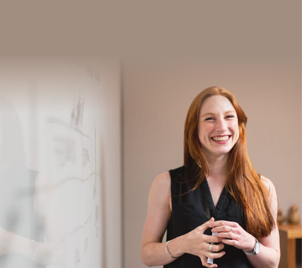 Laughing woman holding a marker in front of a whiteboard covered in notes