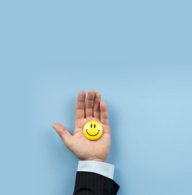 Offene Hand hält einen gelben Smiley-Button vor hellblauem Hintergrund