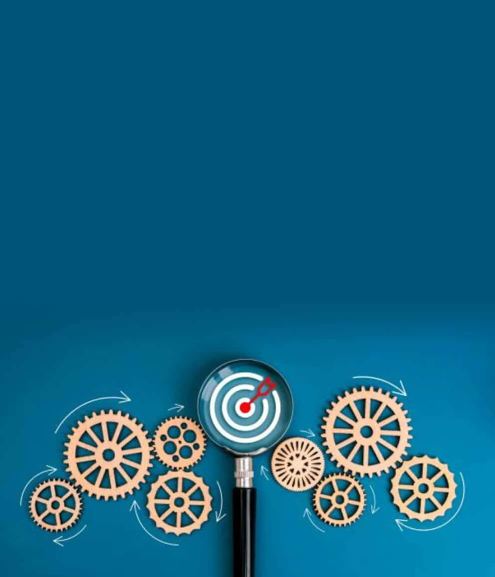 Magnifying glass showing a target among interlocking wooden gears on a blue background