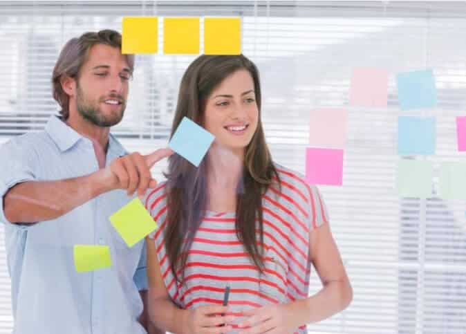 Man and woman arranging colorful sticky notes on a glass wall