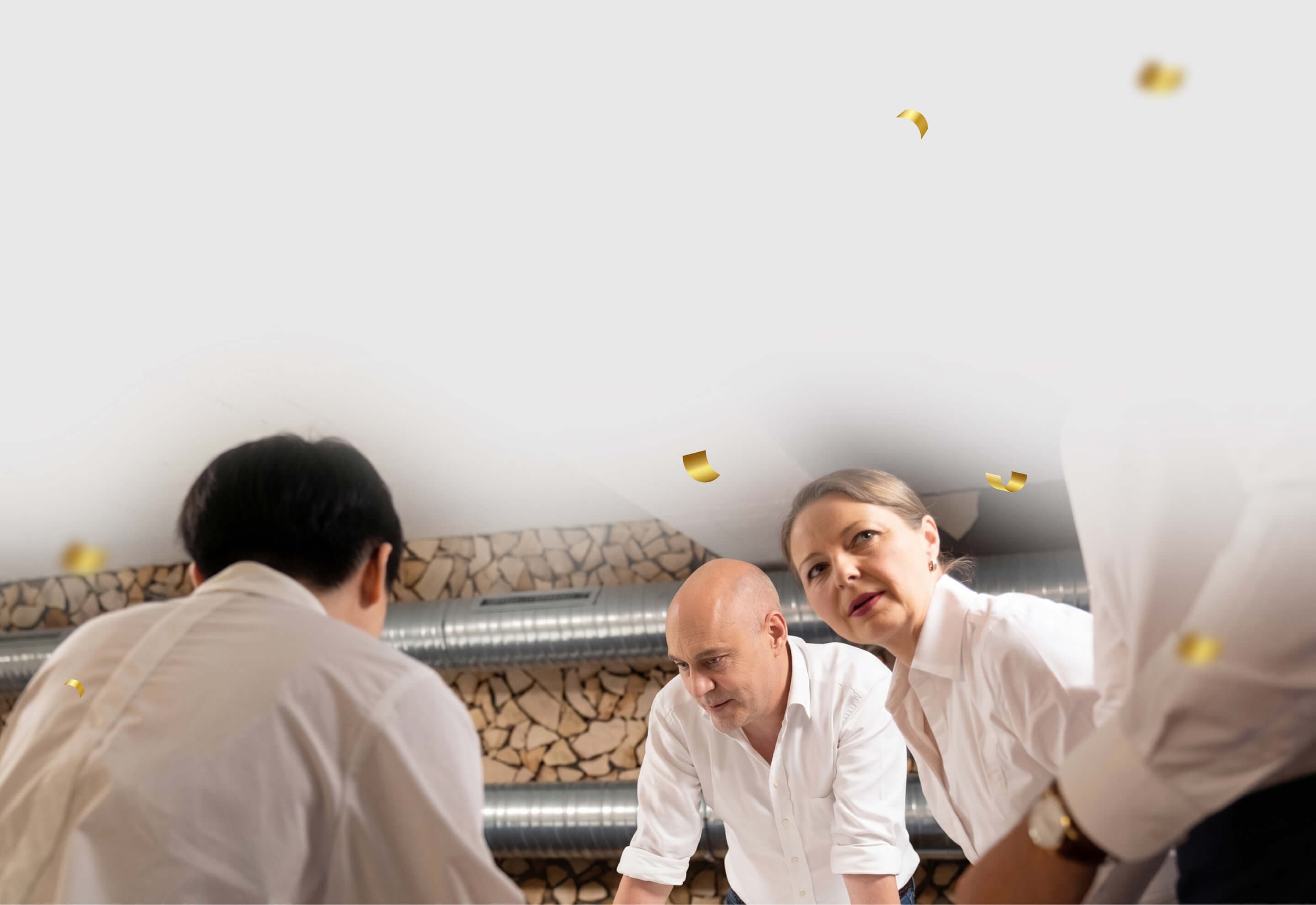 Beratende beugen sich über einen Arbeitstisch, goldenes Konfetti schwebt als Zeichen des Erfolgs durchs Bild