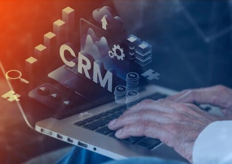 Hände auf einer Laptoptastatur, darüber ein digitaler CRM-Schriftzug mit Diagrammen