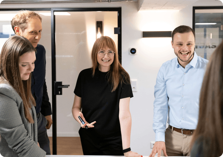 Mitarbeitende stehen lachend an einem Tisch und arbeiten in einem Workshop zusammen