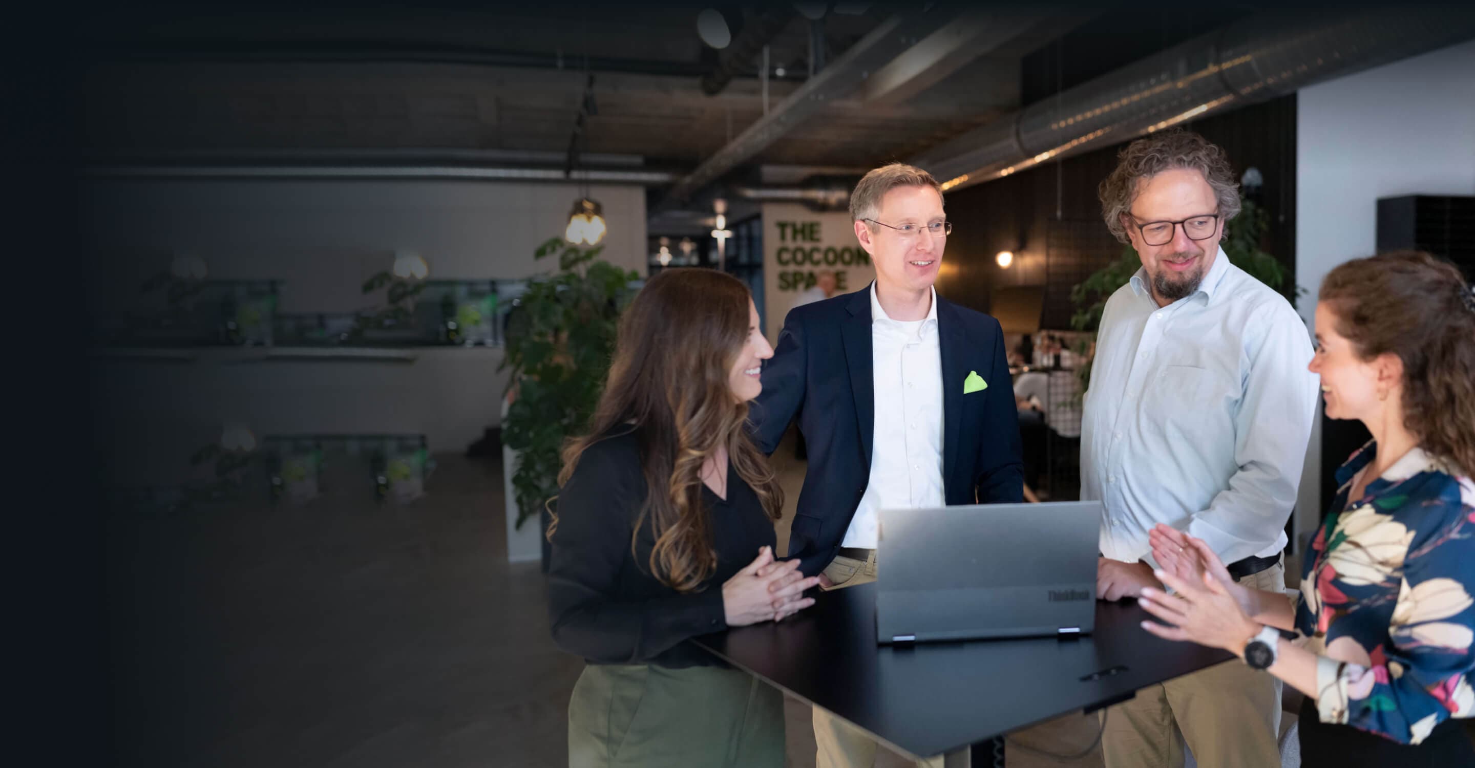 Four consultants at a standing table with a laptop, discussing change management models as a team