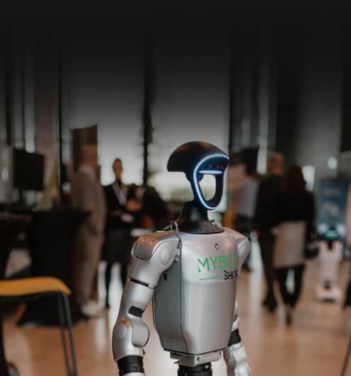 Humanoid robot at a trade fair, with visitors in the background
