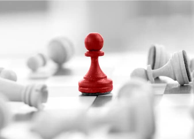 Red pawn standing upright among fallen white chess pieces