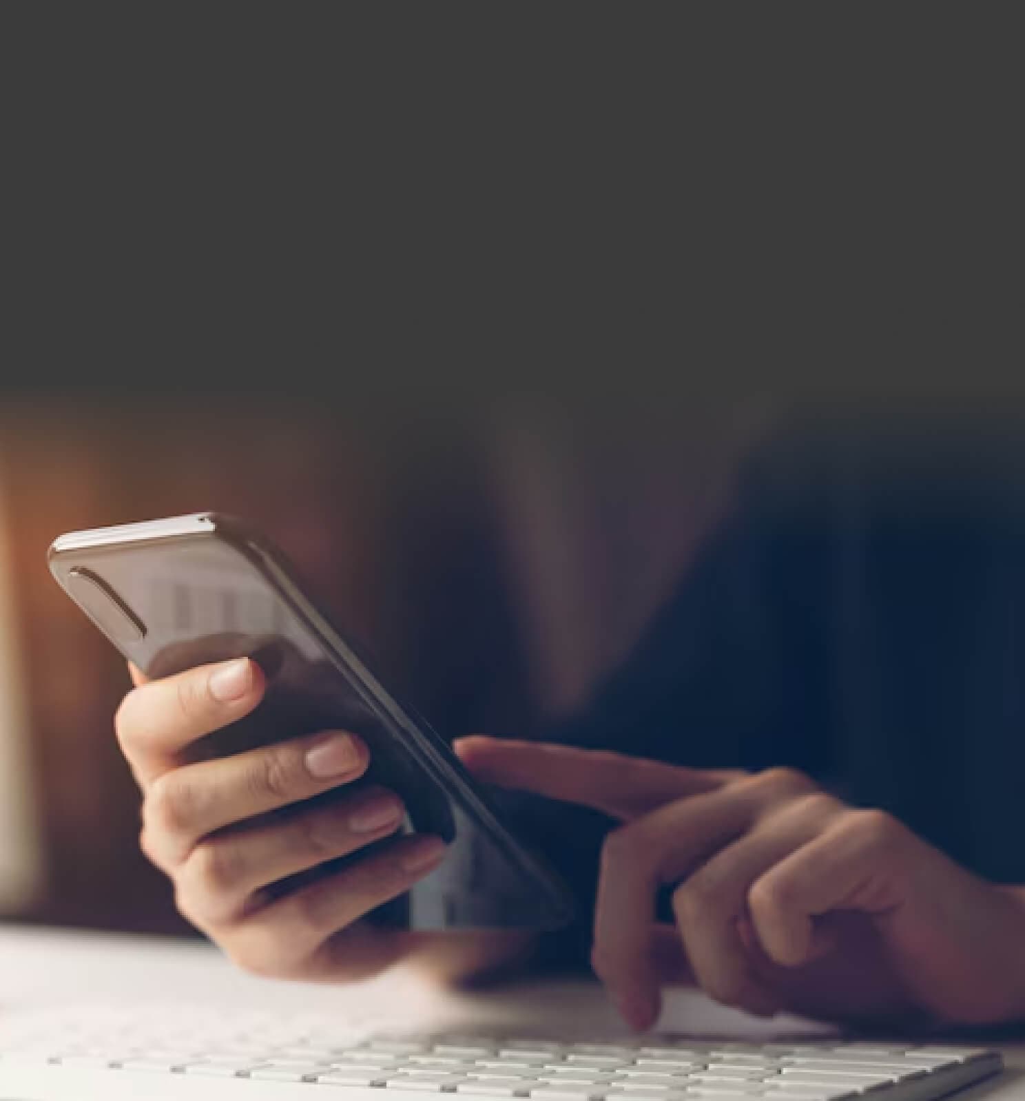 Hands holding a smartphone above a keyboard