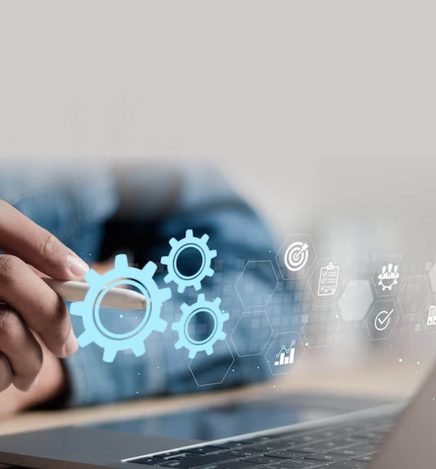 Hand with a pen in front of gear icons above a laptop