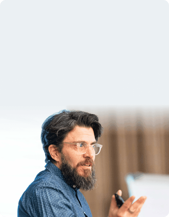 Coach with glasses and a full beard speaking and gesturing to a group
