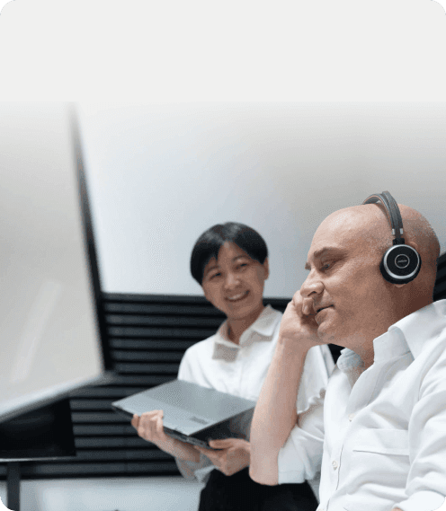 Mann mit Headset am Bildschirm, daneben eine Kollegin mit Laptop – Tagesgeschäft konkurriert mit dem Change-Projekt
