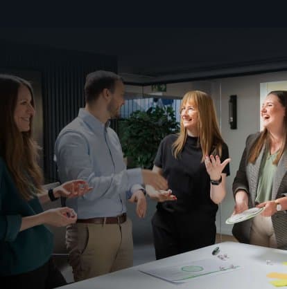 Four colleagues laughing and telling stories at a workshop table with dice and storytelling materials