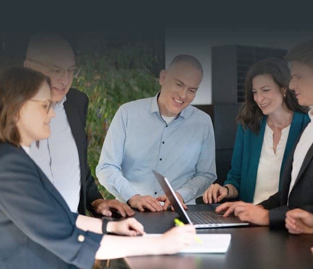 Consulting team standing around a table, looking at a laptop together