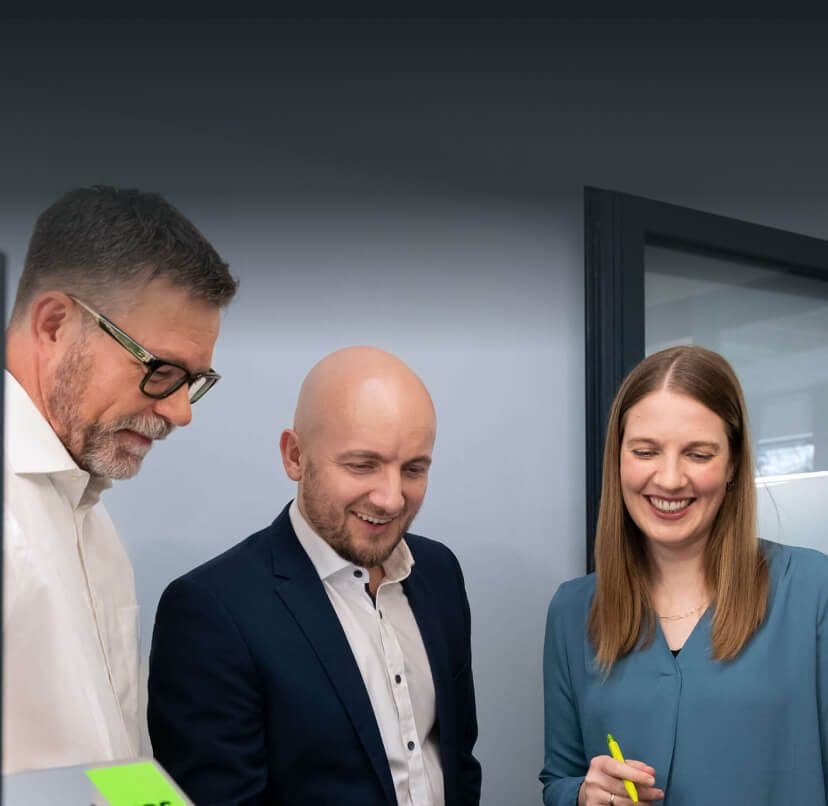 Consultant with a highlighter and two colleagues smiling as they discuss the AI strategy on a laptop