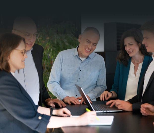 Consulting team standing around a table, looking at a laptop together