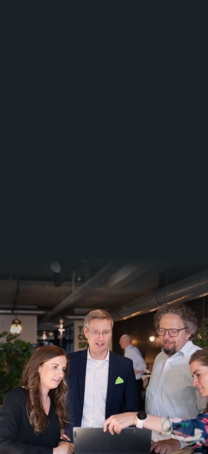 Four colleagues at a standing table discussing content on a laptop
