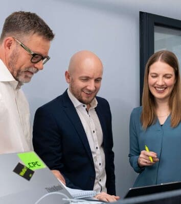 Drei Beratende beugen sich lächelnd über einen Laptop mit CPC-Aufkleber