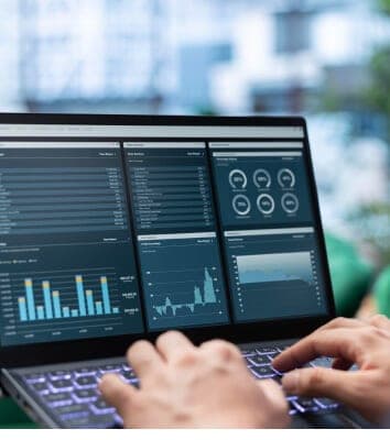 Laptop mit Dashboard aus Diagrammen und Kennzahlen, davor tippende Hände