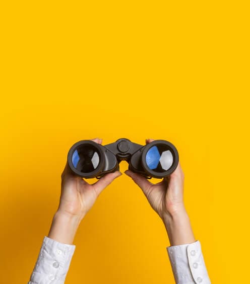 Hands holding binoculars against a yellow background