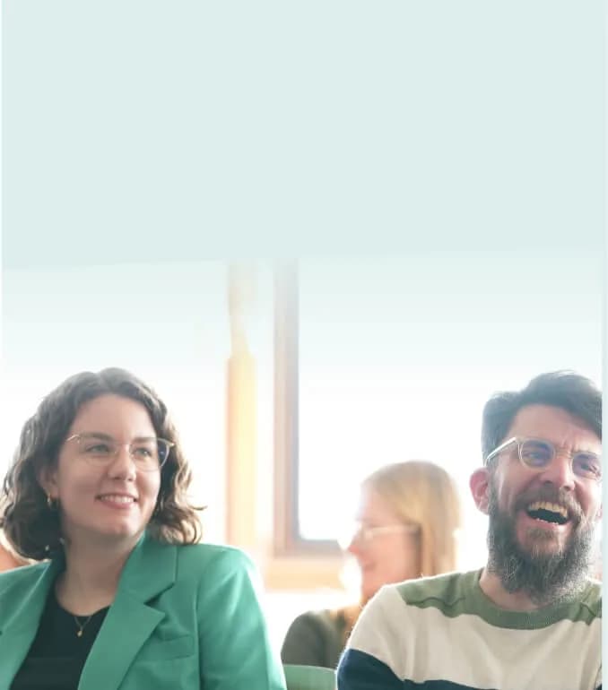 Lachende Teilnehmende sitzen nebeneinander in einem Workshop