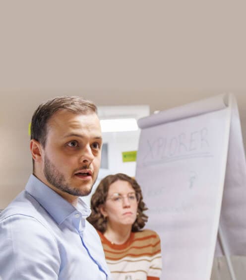 Participant speaking in a workshop, with a colleague and a flipchart behind him