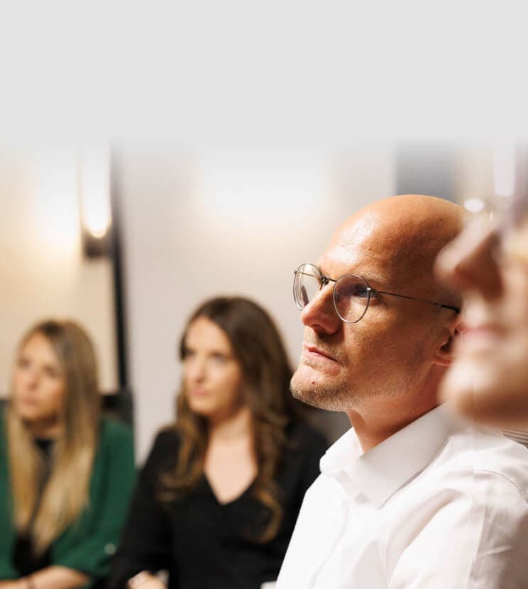 Thoughtful participant with glasses gazing into the distance, two colleagues behind him