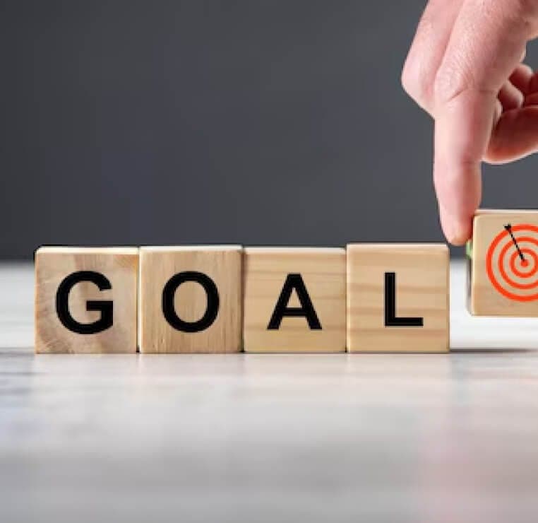 Holzwürfel bilden das Wort „GOAL“, eine Hand setzt einen Würfel mit Zielscheibe dazu
