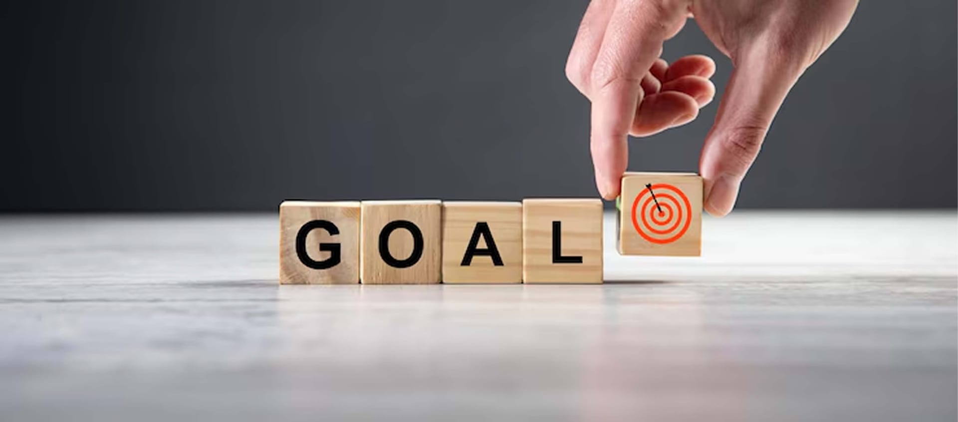 Holzwürfel bilden das Wort „GOAL“, eine Hand setzt einen Würfel mit Zielscheibe dazu
