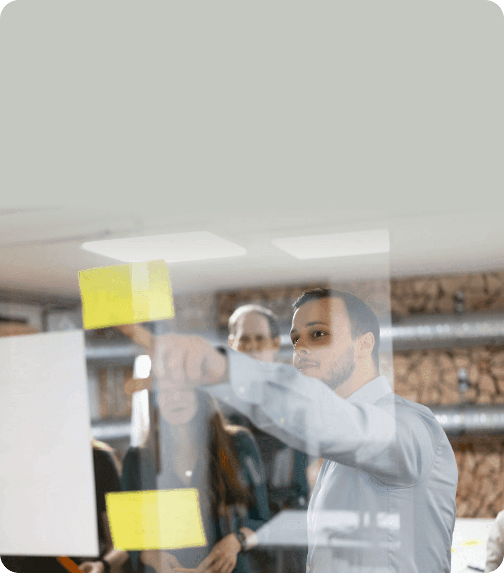 Man putting sticky notes on a glass wall while colleagues look on