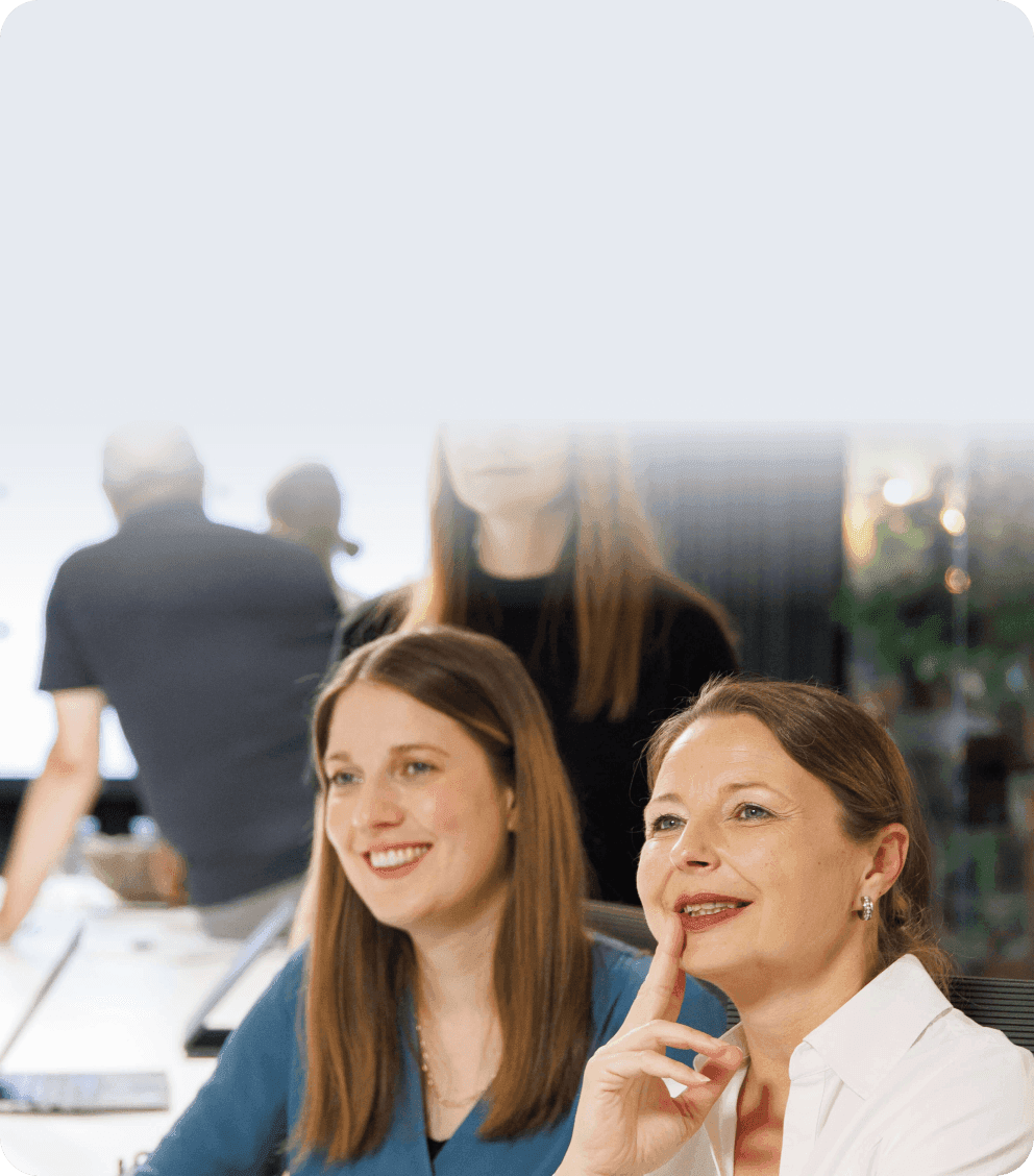 Two women smiling and listening attentively in a meeting
