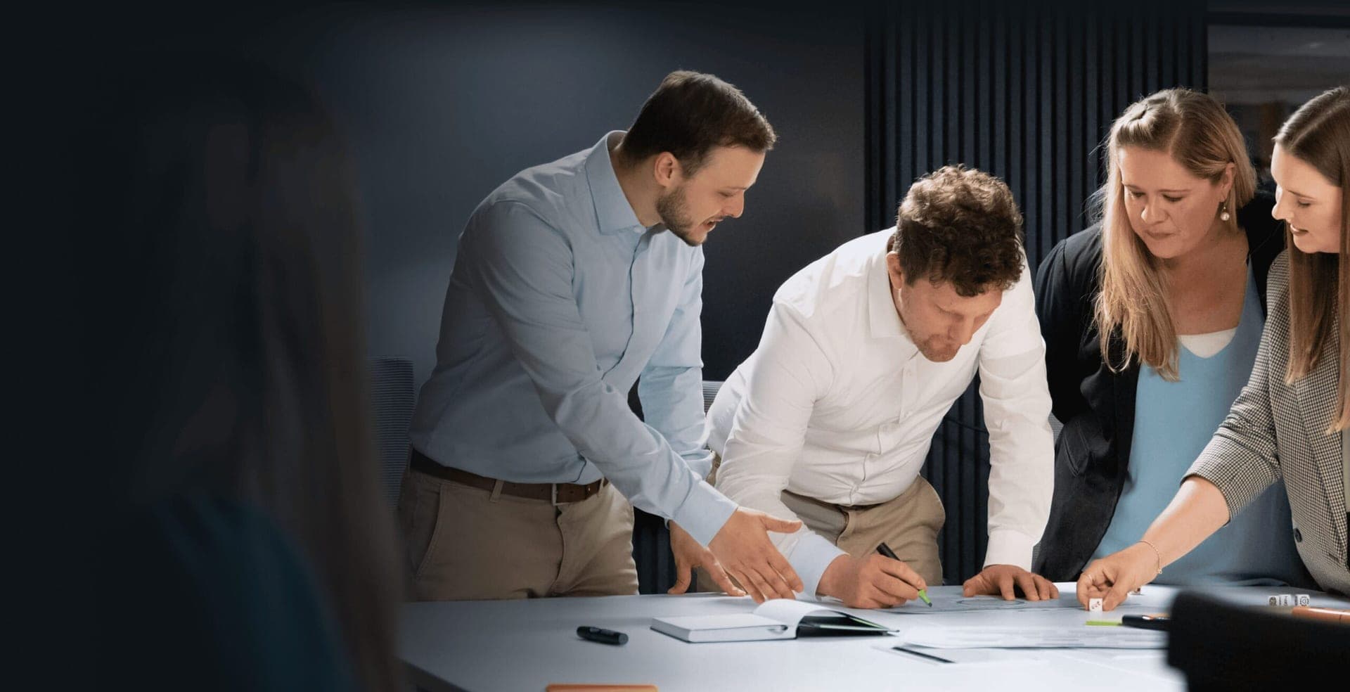 Four colleagues leaning over a table while one of them notes ideas on a large sheet with a marker
