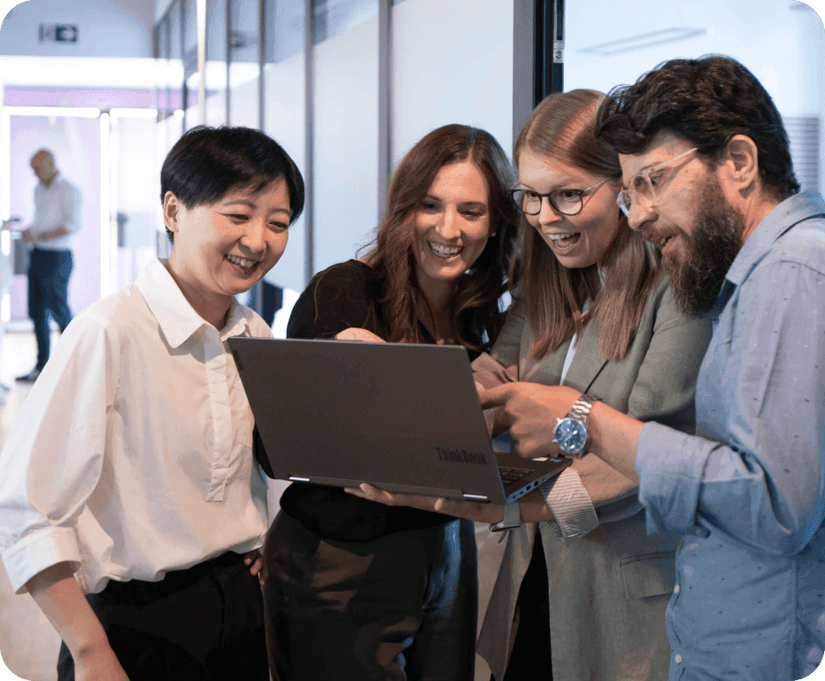 Four colleagues leaning over a laptop, laughing